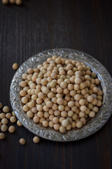 Soybeans in metal plate over black wooden background.