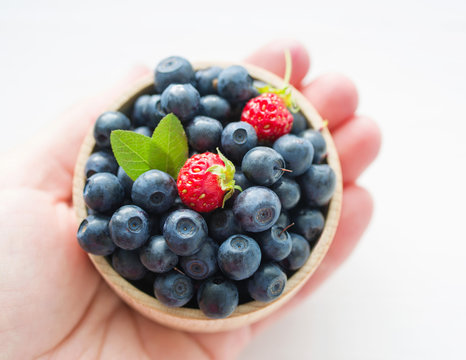 Fresh  blueberries in a wooden cup on a female hand. Close up, top view.
