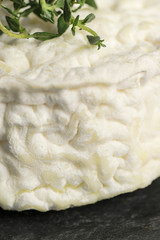 Texture background with part  goat aged cheese and  a branch  of thyme on a dark stone background. Selective focus