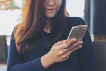 Beautiful Asian woman with smiley face using and looking at smart phone in modern cafe