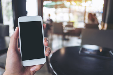 Mockup image of hand holding and raising white mobile phone with blank black screen in cafe