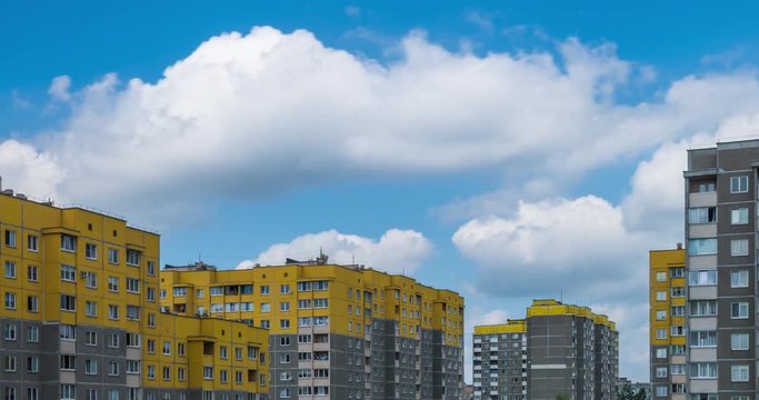 Time lapse clip of white fluffy rolling clouds against the background of yellow multi-storey apartment buildings