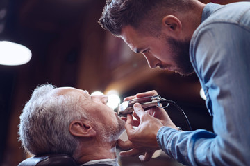 Serious confident barber trimming his clients beard