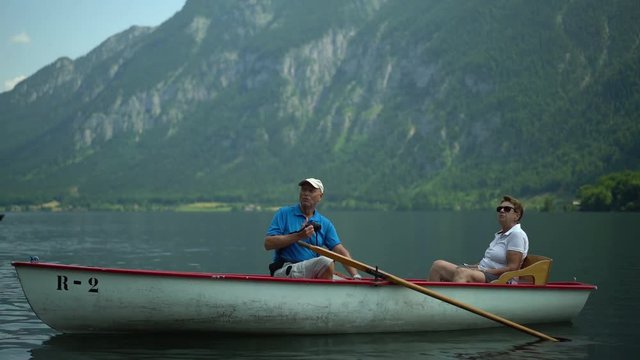 4k travel video, active senior couple sitting in rowboat on austrian mountain lake enjoying landscape and taking pictures
