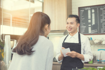 Obraz premium Asian barista man standing for taking order with attractive smiling at coffee shop. Man with owner business concept. 30-40 years old.