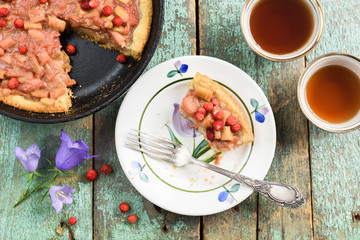 Homemade rhubarb pie with fresh forest strawberries on old turquoise boards with tea and bellflower