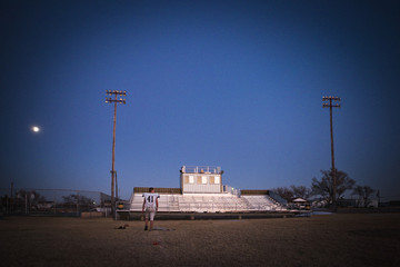 Lone high school football player collecting balls after practice at dusk.