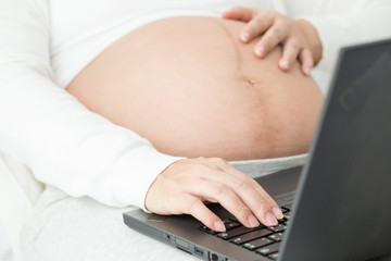 Naklejka premium Pregnant women working at home which online to head office by internet network and vpn to office with black laptop put on her leg