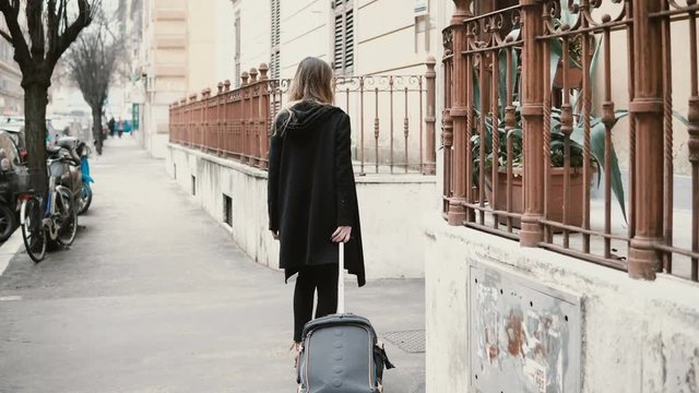 Back view of attractive woman with suitcase walking on the street. Businesswoman are going through the arch.