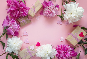 Frame of peonies, gift boxes and decorative hearts on a pink background. Place for text.