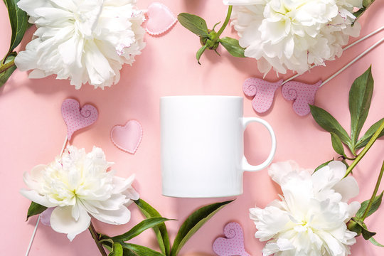 White coffee mug with white peonies and hearts on pink background.