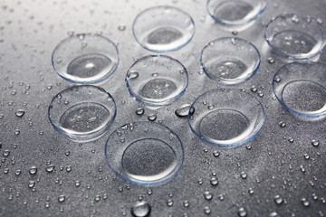 Contact lenses and drops of water on gray background