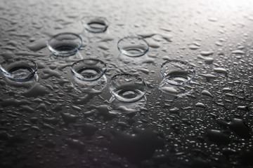 Contact lenses and drops of water on gray background