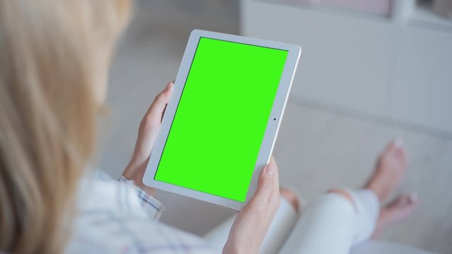 Young Woman in white jeans laying on couch holds Tablet PC with pre-keyed green screen. Perfect for screen compositing. Made from 14bit RAW. 10bit ProRes 444
