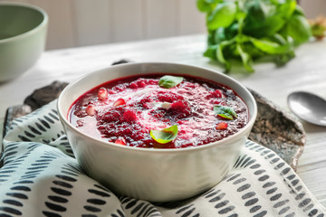Delicious beet soup with sour cream and basil leaves on kitchen table