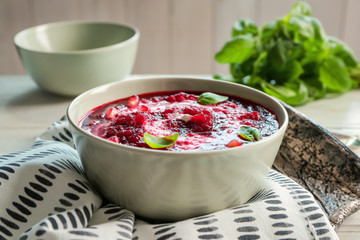Delicious beet soup with sour cream and basil leaves on kitchen table