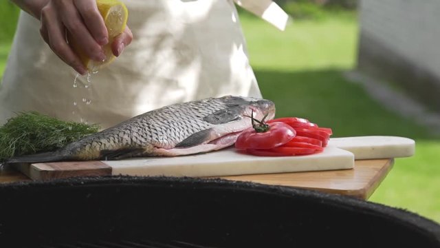 Raw carp is sprinkling with lemon juice in front of the fire of grill, preparations for the barbecue, cooking fish on the open fire, roasted fish, grill and barbecue, cooking outside