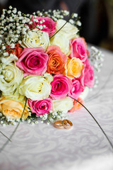 Colorful wedding bouquet made of roses lies before the rings on a table