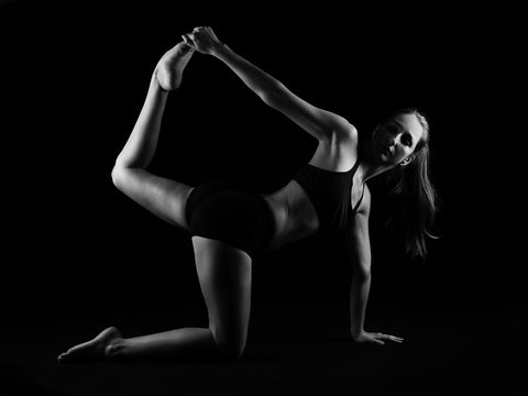 Girl doing yoga stretching on black background
