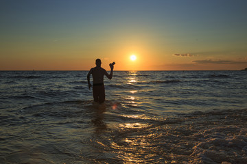 man with a camera walks into the sea at sunset.  professional photographer goes on water to take a photo of the ocean