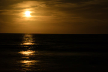 full moon rises over the ocean with a soft orange reflection on the water and the incoming waves