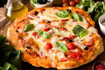 Homemade italian pizza with mozzarella cheese, tomatoes, black olives and basil leaves. Closeup view