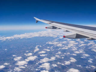 View from a plane window: a plane wing over clouds and blue sky.