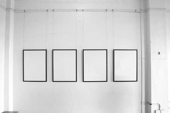 Four vintage empty picture frames hanging from plain white dirty wall.