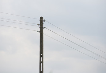 Słup elektryczny stojący na polu trzymający druty przewodzące prąd. Takie kable często padają łupem złodziei  - obrazy, fototapety, plakaty