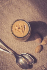 A jar of homemade raw organic almond butter with a fresh salty almonds on the wood board on the brown old rustic wooden background