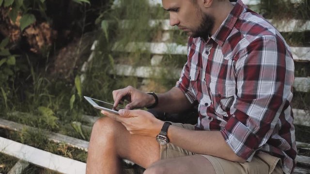 young hipster red bearded man at the park enjoing good weather, red shirt on green background, student doing homework after university lessons