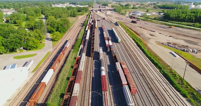 Looking down on industrial railroad rail train yard, many trains, tracks. Dynamic aerial view.