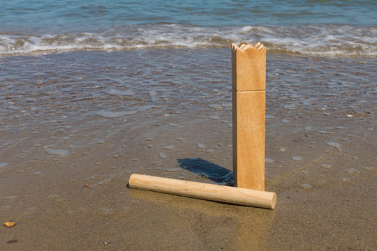 King and a batton from the Swedish outdoor game Kubbs on a beach.