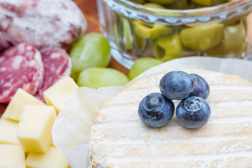 wooden cutting board with cheese, cold cuts and blueberries