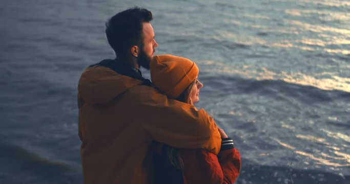 CINEMAGRAPH - seamless loop. Outdoor portrait of young beautiful Caucasian couple enjoying the view of a sunset over the large lake. 4K UHD