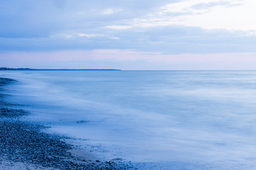 Fototapeta na wymiar Moody empty sea and beach at dusk, pebbles on beach, pastel pink and blue sky