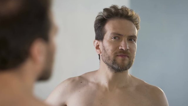 Male narcissist adjusting his hairstyle in front of mirror and brazenly grinning