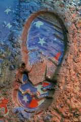 Reflection of the American flag on the footprint of the boot in the ground