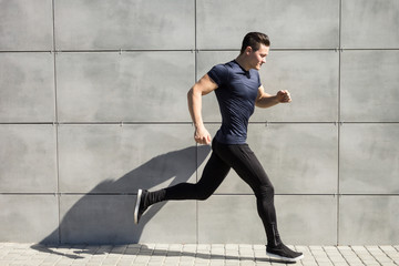 A young man runs against a gray wall, urban.