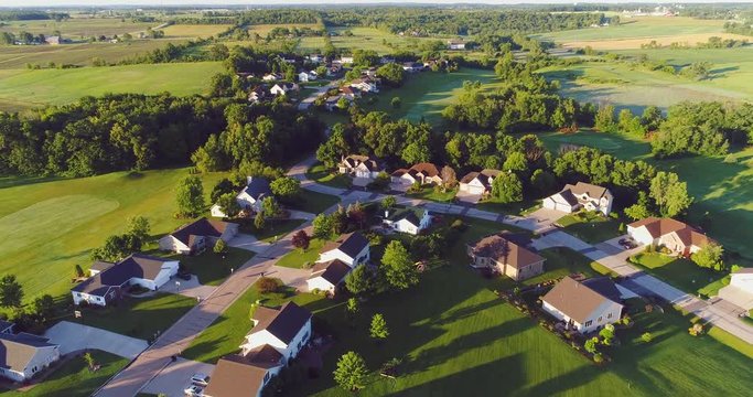 Picturesque rural community amid farm fields and golf course, aerial flyover at sunrise.