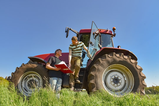 Getreideanbau - Landwirte beraten sich vor einem Traktor auf einem Getreidefeld