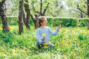 Happy and beautiful girl collects dandelions on a green meadow