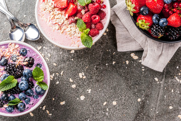 Ideas for healthy summer breakfast. Smoothies in bowls wth red (strawberry raspberry currant), blue (blueberry blackberries) berry With oatmeal, fresh berries. Dark stone table. Top view copy space