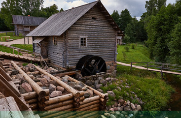 The old water mill/Vintage wooden water mill with the water wheel. Mill made from logs. Visible the stones from which the dam is made. Russia, Pskov region, history