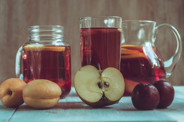 Homemade iced sweet tea with ripe apricots, plums and apples on the rustic wooden background