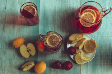 Homemade iced sweet tea with ripe apricots, plums and apples. Homemade tasty lemonade with fresh berries on a rustic wooden background