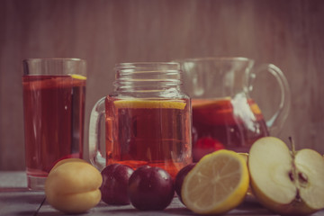 Fototapeta na wymiar Homemade iced sweet tea with ripe apricots, plums and apples. Homemade tasty lemonade with fresh berries on a rustic wooden background