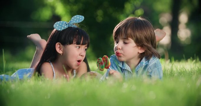 two small children,Caucasian boy and Asian girl having fun in the Park with a Lollipop