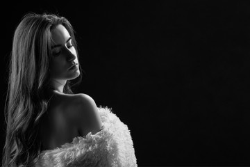 sad woman with bare shoulders in fur on black background, monochrome