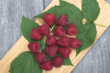 Ripe raspberries on a wooden cutting board and a wooden table